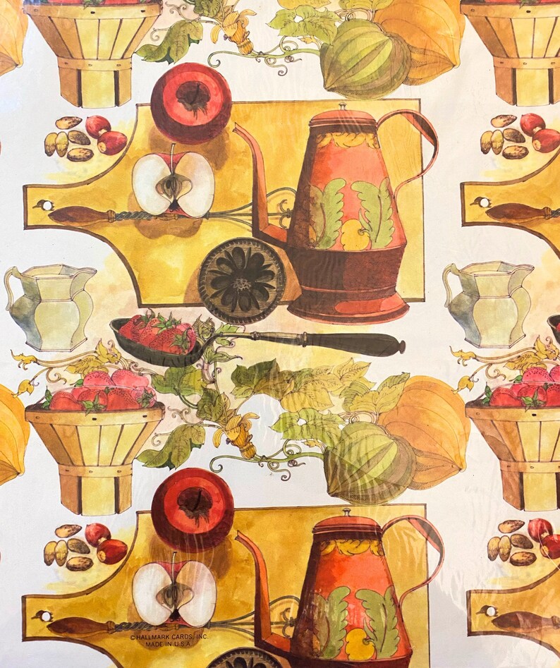 May include: A vintage-style wrapping paper design featuring a repeating pattern of red apples, strawberries, pumpkins, and a brown teapot with green and yellow floral designs. The background is a yellow-gold colour. The text "Hallmark Cards, Inc. Made in USA" is at the bottom of the design.