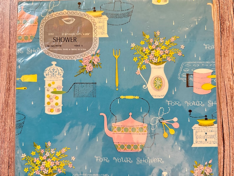 May include: Blue and white wrapping paper with a shower theme. The paper features a teapot, flowers, and kitchen tools. The text "For Your Shower" is repeated on the paper.
