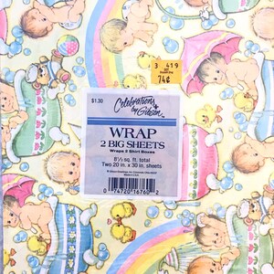 Op de afbeelding: Een geel en roze cadeaupapier met een regenboogontwerp en een patroon van baby's in badkuipen. Het papier is gelabeld "Celebrations by Gibson" en "Wrap 2 Big Sheets". Het papier is 8 1/3 vierkante voet en bevat twee vellen van 20 x 30 inch.