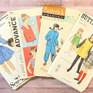 May include: Four vintage sewing patterns for children's clothing. The patterns are from Butterick and Advance. The patterns feature a blue jumpsuit, a yellow dress, a plaid dress, and a red top.