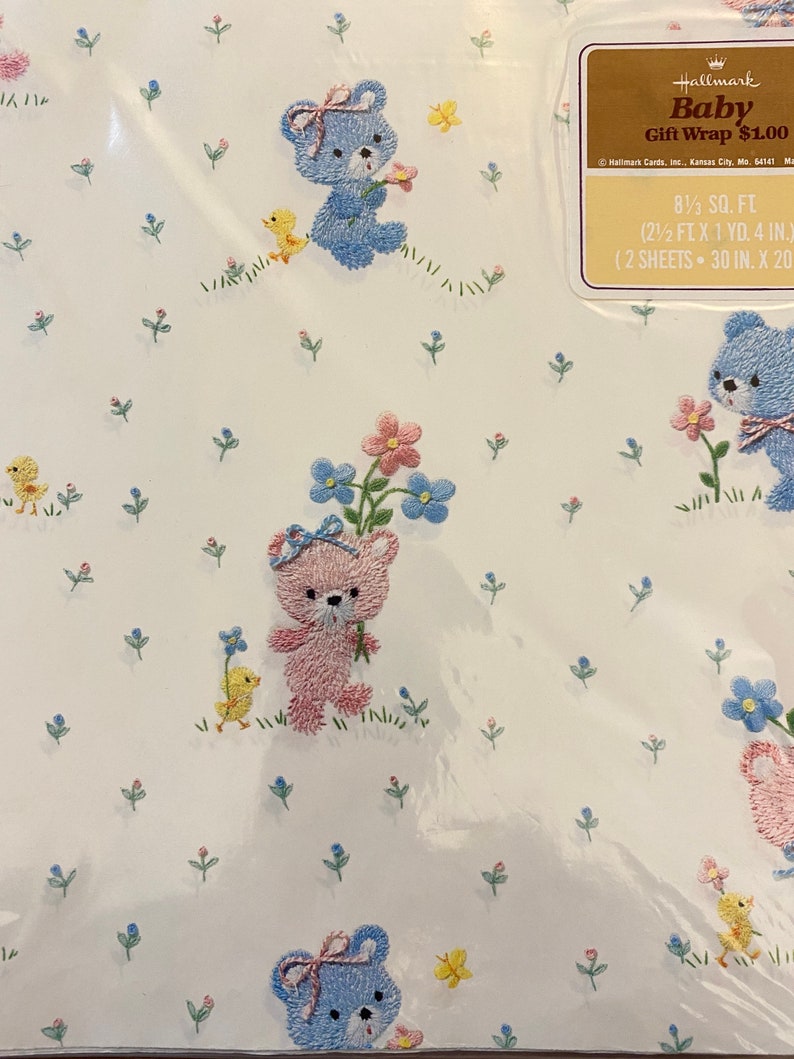 May include: A sheet of baby blue gift wrap with a white background and a repeating pattern of embroidered teddy bears, flowers, and chicks. The text "Baby Gift Wrap &pound;1.00" is printed on the label. 0.77 sq m (2.5 ft x 1 yd. 4 in.) (2 sheets - 76 cm x 51 cm)