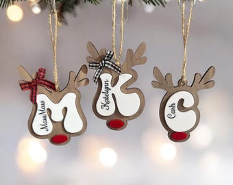 May include: Three wooden reindeer ornaments with white painted faces and red noses. Each ornament has a name written on it: "Katelynn", "Cash", and "Max Maus".