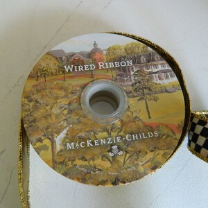 May include: A roll of gold wired ribbon with a black and white checkered ribbon. The ribbon features a printed image of a house and the text "Wired Ribbon" and "MACKENZIE-CHILDS".