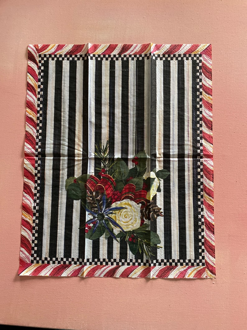 Puede incluir: Una servilleta de tela a rayas blancas y negras con un borde de bast&oacute;n de caramelo rojo y blanco. El centro de la servilleta presenta un dise&ntilde;o floral con bayas rojas, flores blancas y agujas de pino.