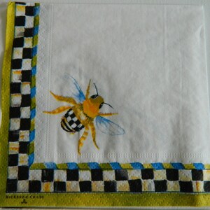 May include: White paper napkin with a black and white chequered border and a green border. The napkin features a yellow and black bee with blue wings.