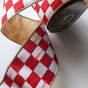 May include: A roll of wired ribbon featuring a red and white checkered pattern. The fabric has a visible brushstroke texture on the red squares and is finished with a metallic gold wire edge along both sides of the length of the ribbon.