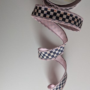 May include: Pink and black checkered ribbon with a pink edge. The ribbon is curled and has a white background.