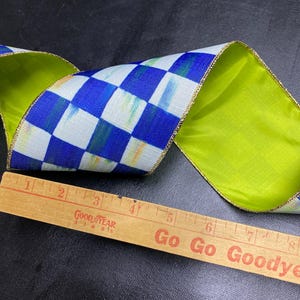 May include: A wired ribbon featuring a blue and white checkered pattern with subtle green and yellow brushstroke accents. The ribbon has a solid lime green underside and gold metallic edges. A wooden ruler shows the ribbon is 4 inches wide.