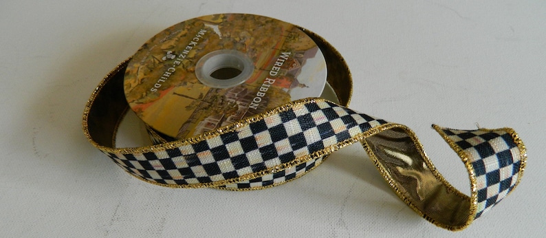 May include: Black and white checkered ribbon with gold trim. The ribbon is wrapped around a spool with the text "Wired Ribbon" and "McKenzie Childs" printed on it.