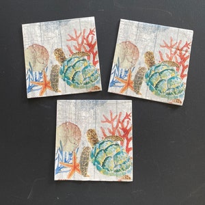 May include: Three white paper napkins with a sea turtle, coral, and starfish design. The napkins feature a light blue, green, orange, and red color scheme.