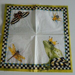 May include: A white paper napkin featuring a green frog wearing a gold crown, a yellow dragonfly, a black and yellow butterfly, and a yellow bee. The napkin has a checkered black and white border with a yellow background.