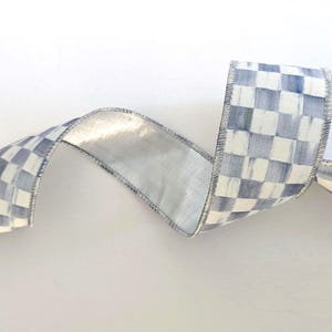 May include: A decorative ribbon with a checkered pattern in shades of blue and white. The ribbon has a metallic silver backing and a stitched edge. The ribbon is curled and displayed against a white background.