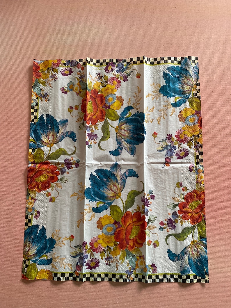 Puede incluir: Una servilleta de papel blanca con un dise&ntilde;o floral con flores azules, rojas, amarillas y verdes. La servilleta tiene un borde a cuadros blanco y negro.