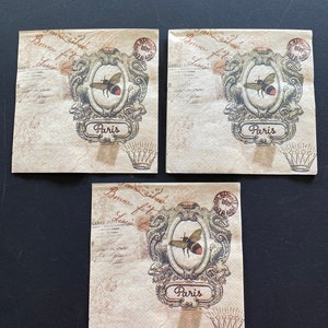 May include: Three decorative paper napkins with a vintage design. Each napkin features a framed bee illustration with the word "Paris" below. The background has script and stamp details, with a crown at the bottom.