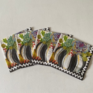 May include: Four white paper napkins with black and white geometric patterns and a floral design featuring succulents and pumpkins.