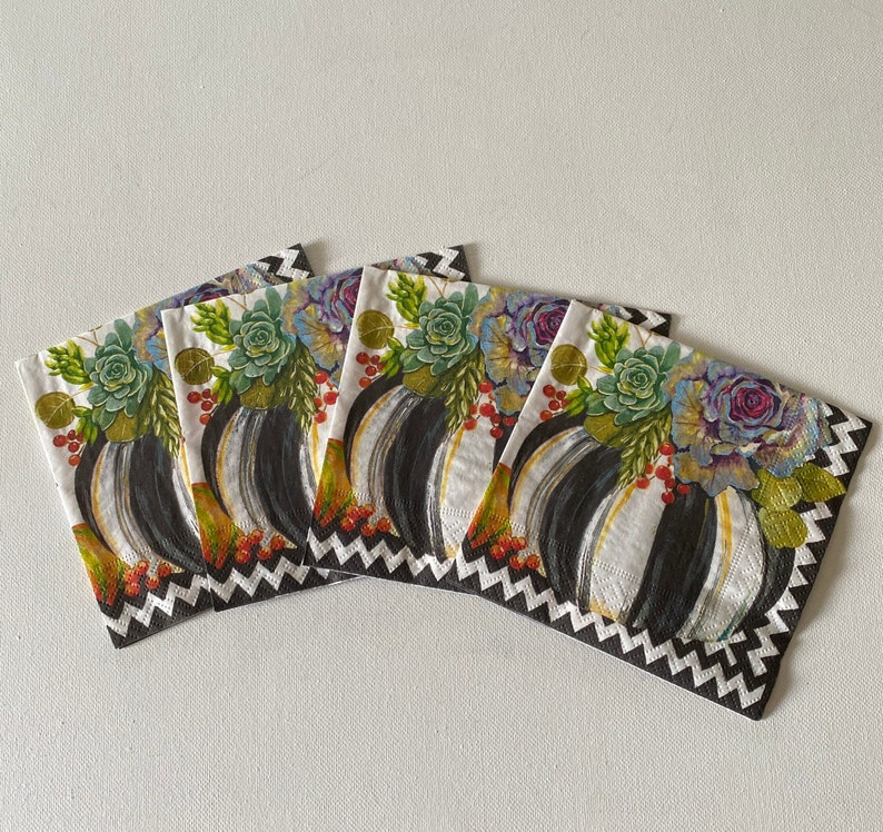 May include: Four white paper napkins with black and white geometric patterns and a floral design featuring succulents and pumpkins.