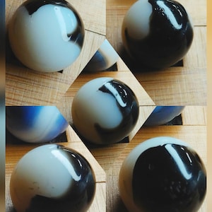 May include: A collection of glass marbles with a swirling pattern of black and white. The marbles have a glossy finish and are arranged on a wooden surface. The marbles are a classic toy.