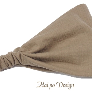 May include: A light brown fabric headband with a gathered knot on one end. The headband is made of a soft, textured fabric. "Hai po Design" is written in brown text on a white background below the headband.