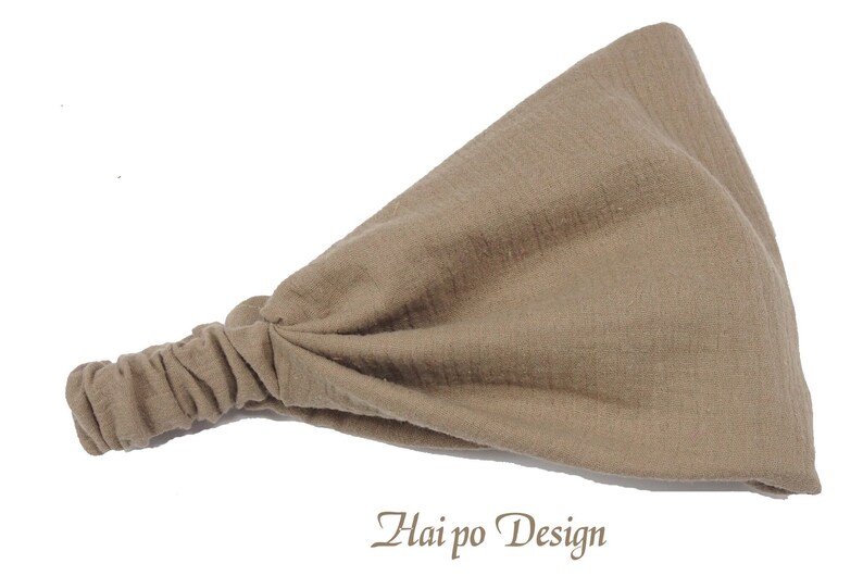 May include: A light brown fabric headband with a gathered knot on one end. The headband is made of a soft, textured fabric. "Hai po Design" is written in brown text on a white background below the headband.