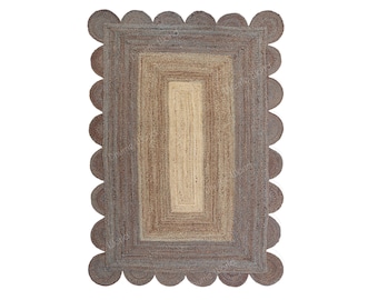 May include: Rectangular jute rug with a scalloped edge. The rug features a gradient design, transitioning from a light beige center to shades of brown and gray at the edges. The natural fibers create a textured appearance.