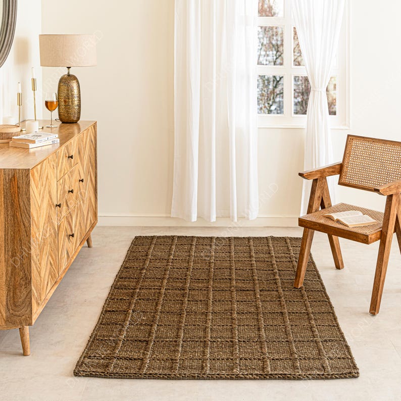 Puede incluir: Una alfombra rectangular de yute marr&oacute;n con un patr&oacute;n de cuadr&iacute;cula se encuentra sobre un suelo claro. La habitaci&oacute;n incluye una c&oacute;moda de madera, una l&aacute;mpara, una silla y una ventana con cortinas blancas. El ambiente es neutro.