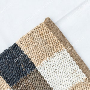 May include: A woven rug with a geometric pattern in shades of beige, black, and white. The rug is made of natural fibers and has a textured surface.