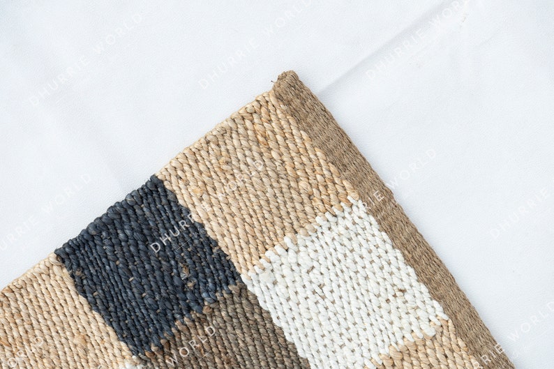 May include: A woven rug with a geometric pattern in shades of beige, black, and white. The rug is made of natural fibers and has a textured surface.