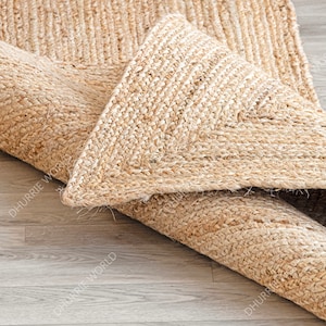 May include: A close-up of a natural fiber rug made from jute. The rug is rolled up and the edges are visible. The rug has a natural, light brown color.