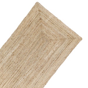 May include: A natural fiber rug made from jute, a sustainable and durable material. The rug has a woven texture and a light brown color. It is a rectangular rug with a fringed edge.