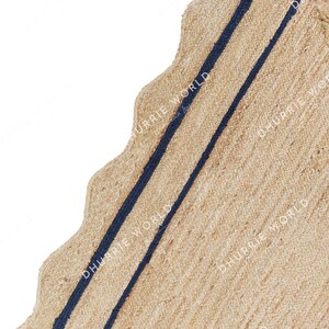 May include: A natural fiber rug with a wavy edge and two navy blue stripes. The rug is made of jute and has a natural, earthy color.