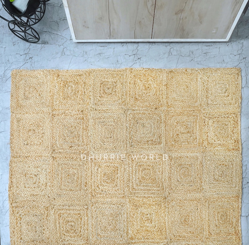 Puede incluir: Una alfombra de fibra natural con un patr&oacute;n cuadrado. La alfombra est&aacute; hecha de yute tejido y tiene un color beige claro. La alfombra est&aacute; compuesta por una serie de cuadrados, cada uno con una textura ligeramente diferente. La alfombra es perfecta para agregar un toque de belleza natural a cualquier habitaci&oacute;n.