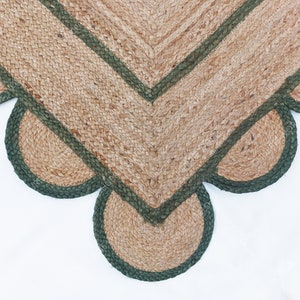 K&ouml;nnte beinhalten: Ein Jute-Teppich mit einem gewellten Rand und einem gr&uuml;nen Saum. Der Teppich ist aus Naturfasern gefertigt und hat einen rustikalen Look.
