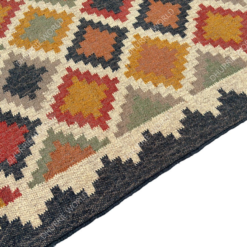 May include: A close-up of a woven rug with a geometric pattern in shades of brown, red, green, and black. The rug has a fringe border.