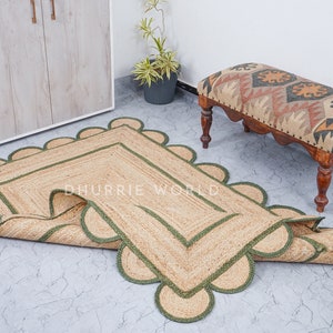 May include: A rectangular jute rug with a scalloped edge and green trim. The rug is rolled up and has a tag that says "Dhurrie World".