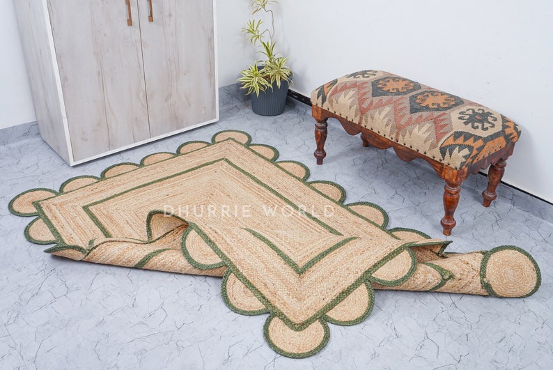 May include: A rectangular jute rug with a scalloped edge and green trim. The rug is rolled up and has a tag that says "Dhurrie World".