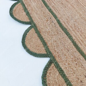 K&ouml;nnte beinhalten: Ein Naturfaser-Teppich mit einem gewellten Rand und gr&uuml;nem Besatz. Der Teppich ist aus Jute und hat eine nat&uuml;rliche, erdige Farbe.