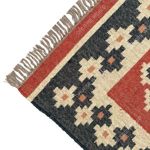 May include: Close-up of a corner of a black, red, and beige patterned rug with fringe. The rug has a geometric design with floral motifs. The text "DHURRIE WORLD" is visible in the image.
