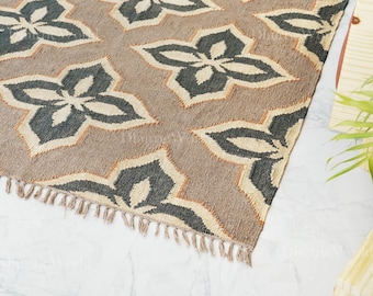 May include: A brown area rug with a repeating floral pattern in gray and cream. The rug has a fringed edge and is made of a woven material. The rug is on a white marble floor.