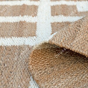 May include: A natural fiber rug with a geometric pattern of white squares on a brown background. The rug is made of jute and has a natural, earthy look.