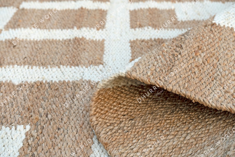 May include: A natural fiber rug with a geometric pattern of white squares on a brown background. The rug is made of jute and has a natural, earthy look.
