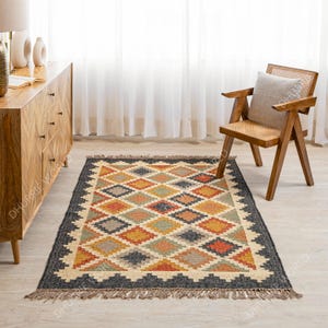 May include: A colorful, geometric patterned rug with a black background and fringe edges. The rug is made of jute and wool and has a hand-woven look.