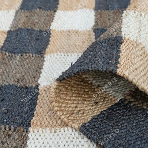 May include: A checkered rug made of natural fibers in shades of brown, beige, and white. The rug is woven in a checkered pattern with a textured surface.