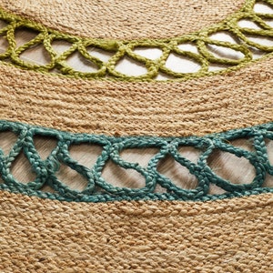 May include: Close-up of a round jute rug with green and teal accents. The rug features a natural, woven texture with decorative openwork borders in green and teal, adding a pop of color to the neutral tones.