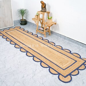 May include: A natural fiber runner rug with a blue scalloped border. The rug is made of jute and has a natural, earthy look. It is perfect for adding a touch of rustic charm to any room.