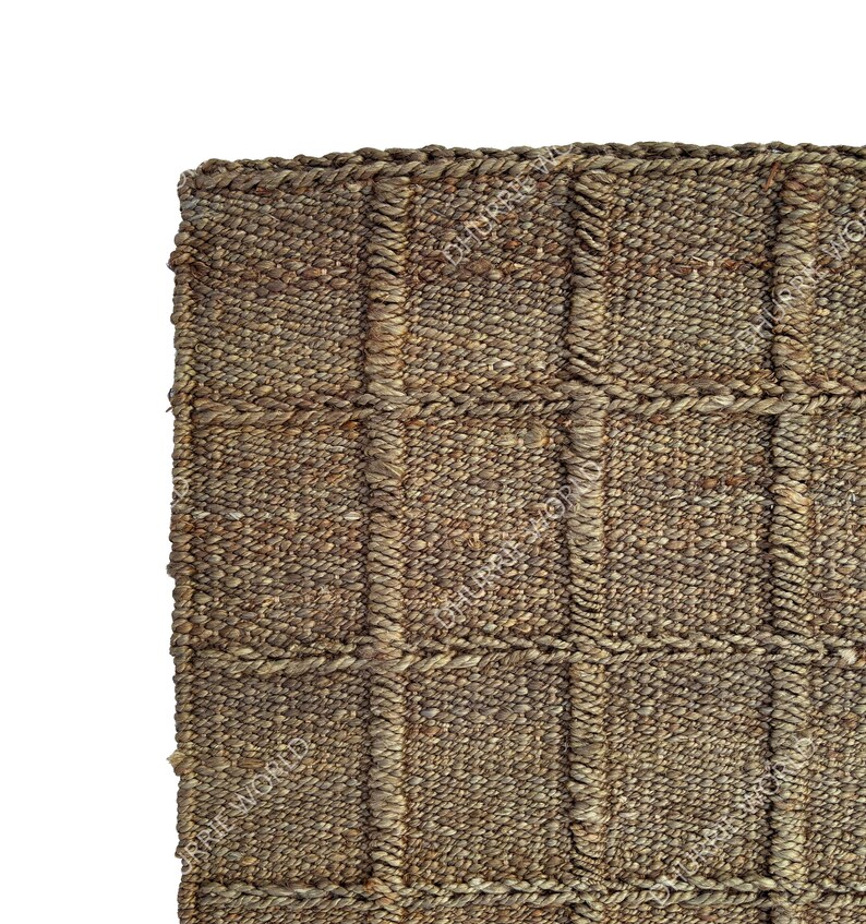Puede incluir: Primer plano de una alfombra tejida con un patr&oacute;n texturizado en forma de cuadr&iacute;cula. La alfombra est&aacute; hecha de fibras naturales en tonos marrones y beige. Los bordes est&aacute;n cuidadosamente acabados, mostrando una est&eacute;tica r&uacute;stica y artesanal.