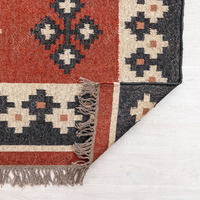 May include: A red, black, and cream colored rug with a geometric pattern. The rug has fringe on all four sides and is folded in half.