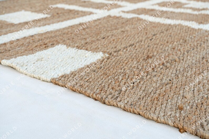 May include: A close-up of a natural fiber rug with a white geometric pattern. The rug is made of jute and has a natural, earthy color.