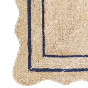 May include: A close-up of a natural fiber rug with a wavy edge and a dark blue border. The rug is made of jute and has a natural, earthy look.
