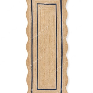 May include: A long, rectangular jute rug with a scalloped edge and a double navy blue border. The rug is made of natural fibers and has a rustic, farmhouse style.