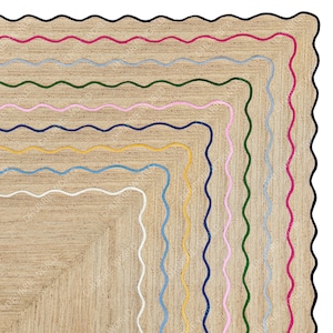 Puede incluir: Una alfombra cuadrada de yute con un borde multicolor. El borde está hecho de líneas onduladas en azul marino, rosa, verde, azul claro, amarillo y blanco.